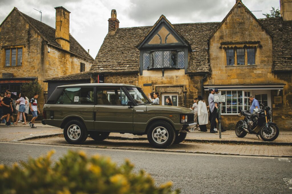 Quaint, charming street in the Cotswolds, England, lined with historic stone cottages, lush greenery, and flower-filled gardens, evoking a picturesque and timeless village atmosphere.